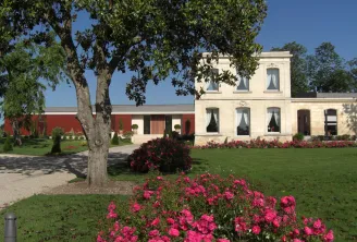 Luchey-Halde Castle in Bordeaux featuring white stone manor house, red building, manicured gardens with pink flowers and ancient tree