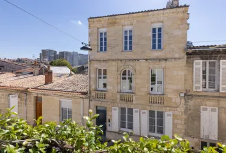 Stone-built classical building in the Séraphines district of Bordeaux, featuring a symmetrical façade with blue windows and balustrades, surrounded by modern buildings.