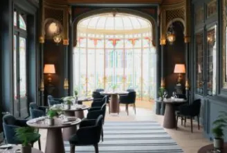 Elegant interior of Grand Barrail restaurant in Bordeaux featuring ornate gilded ceiling, arched bay window, round tables, black chairs and refined decor