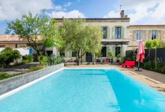 Charming stone house with rectangular turquoise swimming pool, paved terrace, olive trees, red umbrella and traditional architecture near Bordeaux