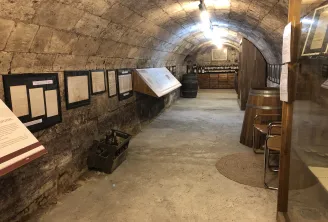 Stone vaulted cellar interior with informational panels on the walls, wooden barrels, displayed wine bottles, and winemaking equipment at the Bordeaux Wine and Trade Museum.