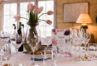 Elegantly set dining table at Siaurac in Bordeaux featuring wine glasses, gold cutlery, printed menu, and pink tulips in a vase near a bright window.