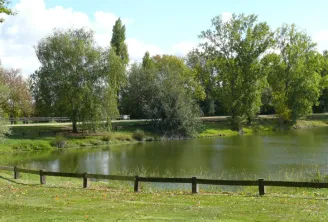 View of Cantefrêne Park in Bordeaux featuring a pond surrounded by trees, a wooden fence in the foreground, and green lawns.