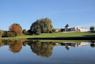 Château Paveil de Luze near Bordeaux reflected in a still pond, featuring the white classical mansion, autumn trees, and manicured green lawn under a clear blue sky.