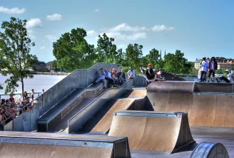 Bordeaux skate park featuring concrete ramps with skaters and spectators, overlooking the Garonne River and city architecture