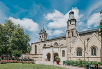 Basilica of Saint-Seurin in Bordeaux, a white stone religious building with two towers, surrounded by greenery and a landscaped square under a clear blue sky.