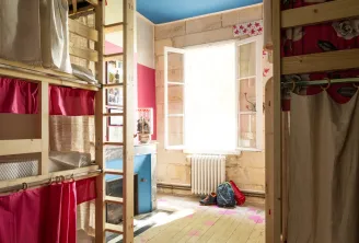 Dormitory room at Les Joalles in Bordeaux featuring wooden bunk beds, red and beige curtains, bright window, blue ceiling and light wooden floor