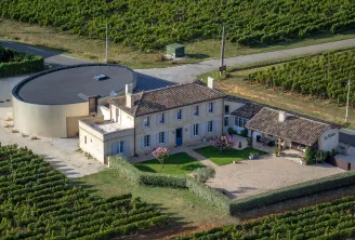 Aerial view of Château La Voûte near Bordeaux, featuring the main residence with blue shutters, surrounding vineyards, and a modern circular water tank.