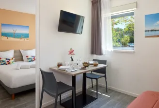 Modern hotel room in Bordeaux featuring a comfortable bed, work desk, black chairs, wall-mounted TV, window with garden view, coastal décor, and contemporary furnishings.