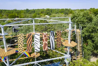 Aerial view of a platform with animal-patterned fabrics hanging on a metal structure, overlooking dense forest at Cimes de Bordeaux in Pessac.