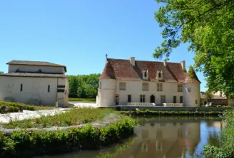 Cayac Priory near Bordeaux, a Jacobean complex featuring a white stone main building with red tiled roofs, an adjoining fortified mill, and a small canal in the foreground reflecting the structures amid lush greenery.