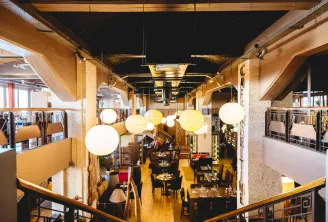 Interior view of Café Maritime in Bordeaux, featuring a modern restaurant with wooden beams, suspended spherical lights, black tables and wooden chairs, side galleries, and warm evening lighting.