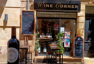 Storefront of Wine Corner, a wine bar in Bordeaux, featuring a display window with wine bottles, outdoor seating with high chairs, chalkboard menu and signage.