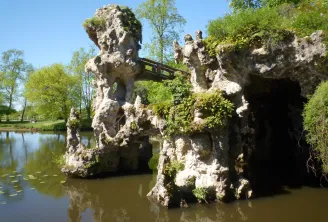 White stone ruins with a moss-covered arch beside a pond, surrounded by lush green vegetation in Majolan Park, Bordeaux.