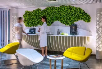 Modern reception area of Spa Dock G6 in Bordeaux featuring a green living wall, ribbed white counter, yellow designer chairs, and two staff members in white uniforms