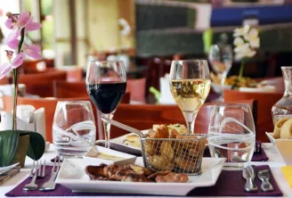 Elegantly set dining table at Soretel Bordeaux Mérignac restaurant featuring red and white wine glasses, charcuterie plate, bread basket, pink orchid and refined décor