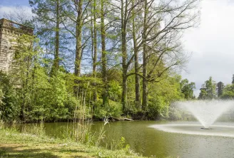 View of Bourran Park in Bordeaux featuring a historic stone tower, a lake with fountain, majestic trees and lush spring vegetation.