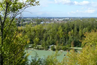 Panoramic view of Parc de l'Ermitage Sainte-Catherine in Bordeaux featuring a lake in the foreground, poplar forest, and city skyline under a cloudy sky