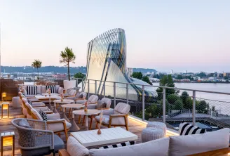 Luxury rooftop terrace in Bordeaux featuring modern woven furniture, overlooking the Garonne River with the Cité du Vin architecture visible at dusk