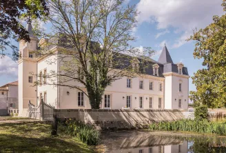 Château Sénéjac, an elegant white mansion with turrets and slate roofs, surrounded by trees and a moat, near Bordeaux.