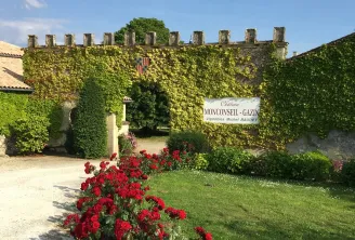 Château Monconseil-Gazin in Bordeaux with ivy-covered stone walls, red rose bushes in the foreground, and a vineyard sign