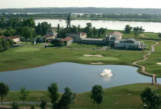 Aerial view of Margaux Golf Club near Bordeaux, featuring greens, bunkers, a pond in the foreground, and clubhouse buildings in the background overlooking the Garonne valley.
