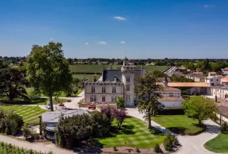 Aerial view of Château Pape Clément in Bordeaux, a white neo-gothic castle surrounded by formal gardens and vineyards, under a clear blue sky.