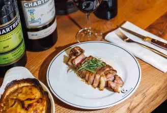 Sliced duck breast plated with fresh greens and vegetables, paired with Bordeaux wines and potato gratin in a fine dining restaurant.
