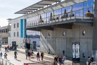 Modern facade of Cap Sciences in Bordeaux featuring large glass windows, green terrace, and busy public square with visitors and cyclists