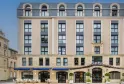 Facade of Hotel Burdigala by Inwood Hotels in Bordeaux, a Haussmann-style building with a commercial ground floor featuring blue storefronts and terrace, topped by six office floors with regular windows and an attic story with arched dormers.