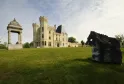 Old Lormont Castle in Bordeaux featuring crenellated stone towers surrounded by green lawns and contemporary sculptures under a partly cloudy sky