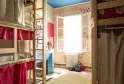 Joualles dormitory in Bordeaux: spacious bedroom with wooden bunk beds, red and beige curtains, bright window overlooking the street, blue ceiling, light wooden floor.