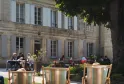Three striped deckchairs on the lawn of Château Ambe Tour Pourret garden in Bordeaux, with visitors sitting in the background in front of the stone façade.