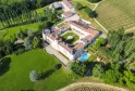 Aerial view of Château Toulouse-Lautrec near Bordeaux, featuring a white castle with towers surrounded by green gardens, a swimming pool, vineyards, and forested areas.