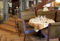 Elegant dining room of Le Bordeaux restaurant featuring striped blue and gold armchairs, a set round table, wooden staircase, and historical displays on the walls.