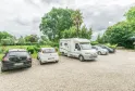 Motorhomes and cars parked at Château Beau Rivage in Bordeaux, surrounded by green trees under a cloudy sky