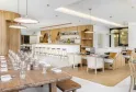 Modern interior of Bistrot Le Saint-Jean in Bordeaux featuring a wooden bar, natural wood tables, white chairs, contemporary pendant lighting, and minimalist warm and white décor.