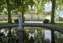 Château Siran in Bordeaux reflected in a pond, surrounded by ancient trees with a stone statue in the foreground