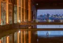 Night view of Bordeaux's submarine base featuring illuminated orange columns reflected in still water, overlooking the port and Garonne river at dusk.