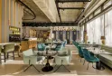 Modern and bright interior of Bada restaurant in Bordeaux featuring turquoise and green seating, black tables, wooden bar, large windows, industrial ceiling and gold geometric decor.