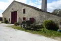 Stone building with burgundy doors and windows, wooden-wheeled cart in front of the facade, chimney in the background, Château de Lisennes near Bordeaux