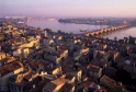 Aerial view of Bordeaux at sunset showing the old town rooftops, the Stone Bridge spanning the Garonne River, and the quays bathed in golden light