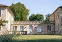 Courtyard view of Château de Ferrand in Bordeaux featuring stone buildings with balustrades and green lawn under clear blue sky.