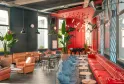 Modern lounge space in Bordeaux featuring red and teal walls, orange and red armchairs, blue chairs, gold hanging lights, green plants, and contemporary furniture in a vibrant urban setting.