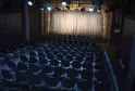 Empty theater auditorium with rows of black seats facing an illuminated stage with white and gold curtains in Bordeaux