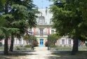 Facade of Château Saint Ahon in Bordeaux, a pink and white building with a blue door, framed by ancient trees and a paved pathway.