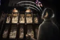 Visitor wearing headphones viewing the illuminated bronze doors of the Basilica of Saint-Seurin in Bordeaux at night, featuring detailed religious sculptural scenes.
