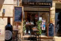 Storefront of Wine Corner, a wine bar in Bordeaux, featuring wine bottles on display, outdoor seating with high tables, and promotional signage.