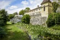 Château Beauregard in Bordeaux featuring stone facades, pointed tower, and water lily pond in the foreground, surrounded by lush greenery
