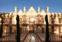 Facade of Mondrian Bordeaux Les Carmes, a historic Neo-Renaissance building featuring crenellations, turrets and ornate windows, framed by two green cypress trees and a paved courtyard in Bordeaux.
